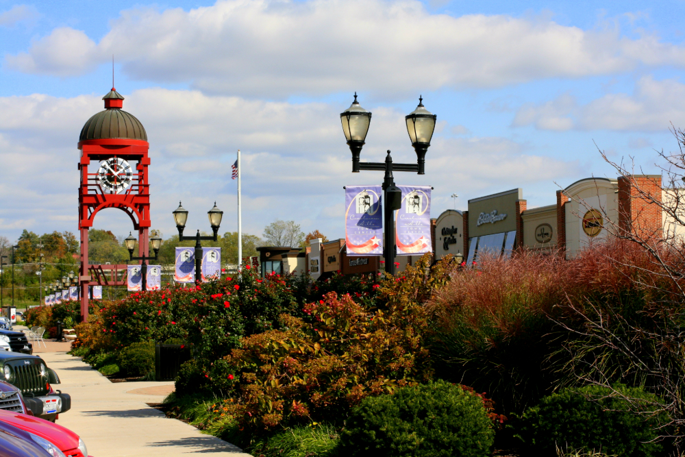 Red clock tower on a shopping plaza, with banners on lampposts and storefronts in the background.