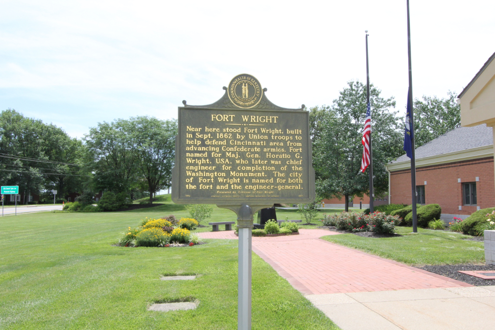 Historic bronze marker about Fort Wright on a grassy lawn with a flagpole and brick building in the background.