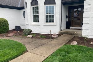 White brick house with arched windows, front door with wreath, and a curved concrete walkway through a landscaped yard.