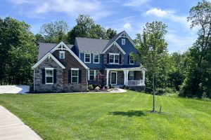 Two-story house with stone and blue siding, white trim, and a manicured front lawn on a sunny day.
