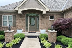 Brick front entrance with a double front door, stone path, and landscaped pillars and shrubs on either side.